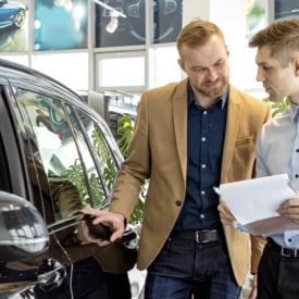 Two men standing in car dealership next to a black car and talking